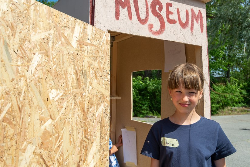 En flicka står framför ett lådhus med texten museum.